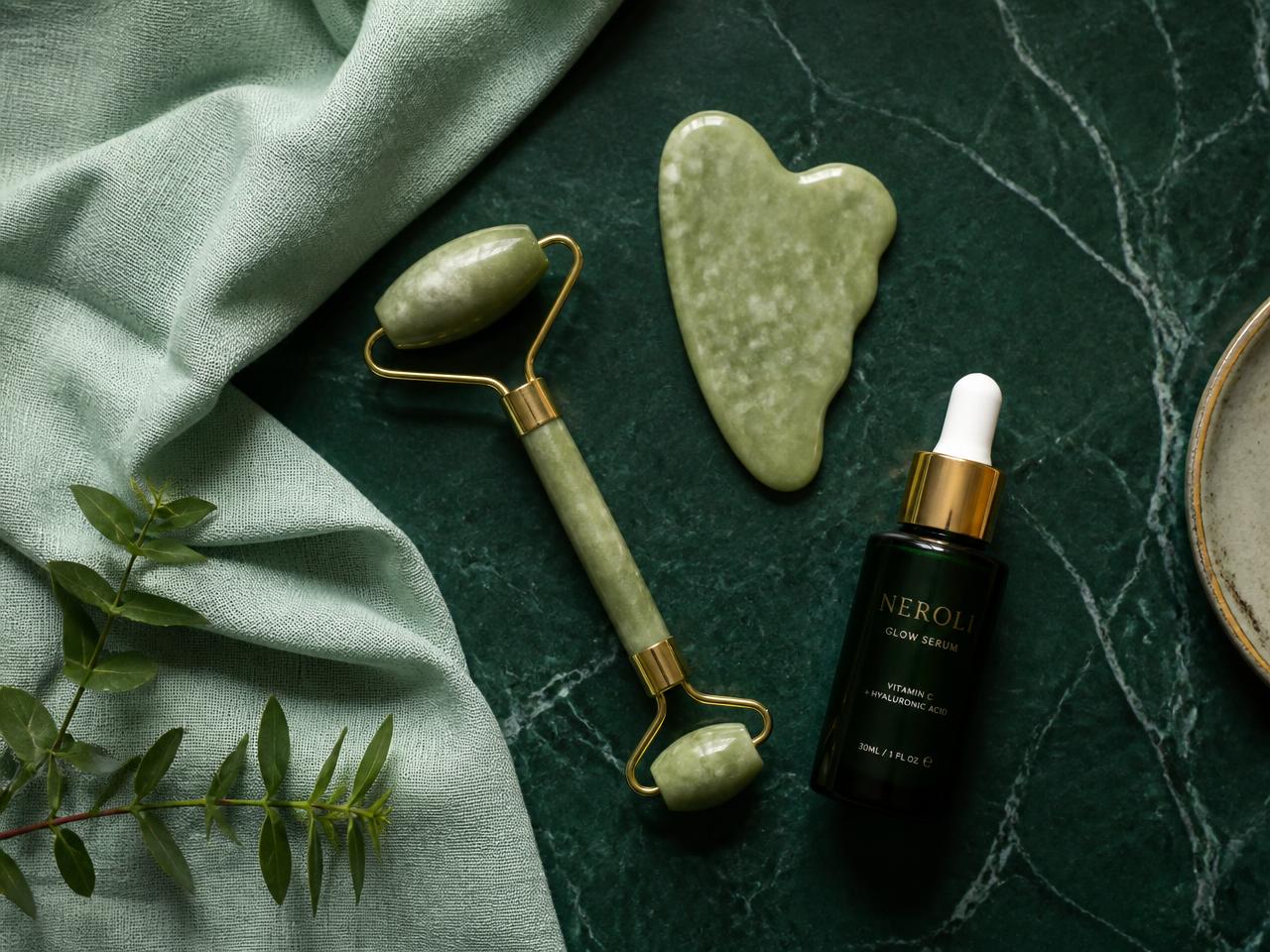 Gua Sha, rodillo de jade y sérum facial sobre mármol verde